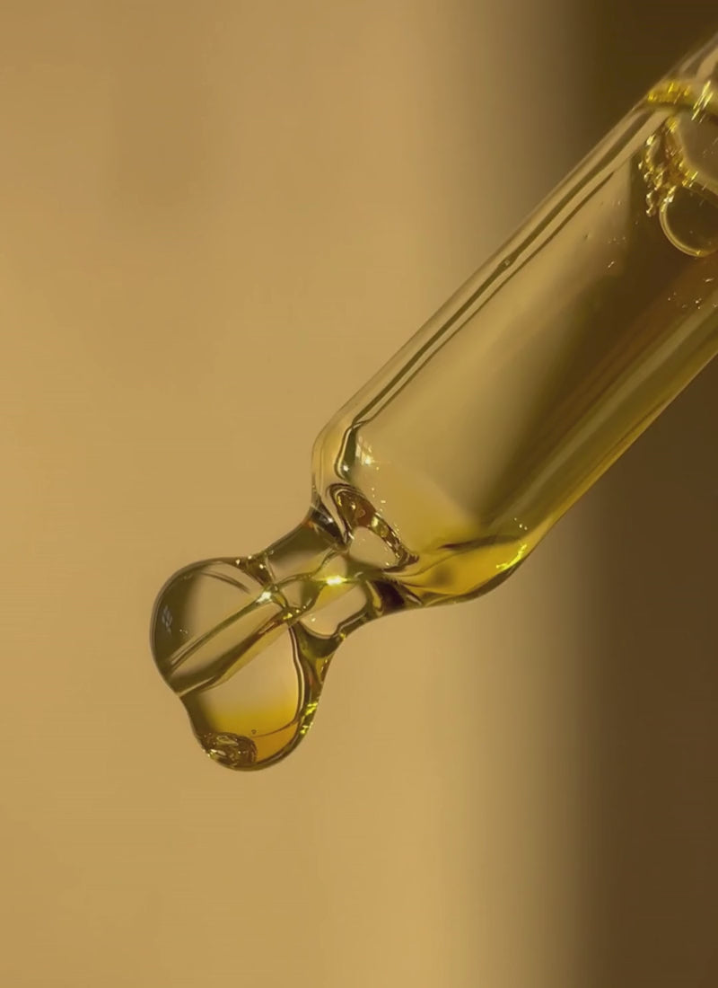 Golden face oil dropper with a single drop forming, showing smooth liquid texture